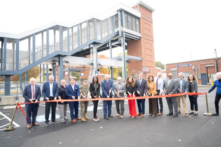 The image shows a group of people cutting a ribbon at the Quantico Station, marking the completion of station improvements.