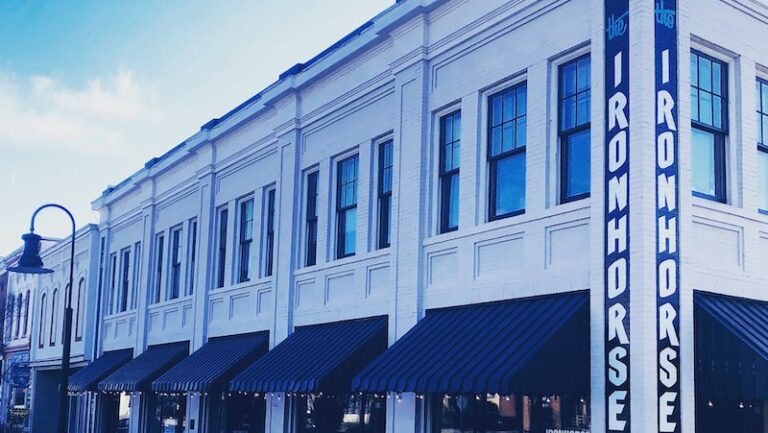 A white brick building with large windows, featuring striped awnings and a sign that reads "IRONHORSE."