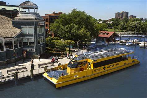 A yellow water taxi docked by the shore with people nearby, surrounded by greenery and buildings.